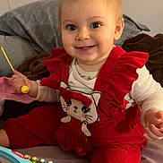 Lilas a rejoint le concours — aidez-le/la à gagner de superbes lots ! toddler, child, smiling, red_overalls, cat_design, toy, xylophone, indoors, bed, blanket, happy, cute, playtime, person, baby, foot, hand, face, clothing, room