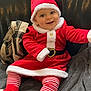 baby, child, santa_claus_costume, red_clothing, striped_leggings, smiling, indoor, couch, blanket, festive, holiday, cute, happy, portrait, infant, headwear, cozy, plush, person, seasonal
