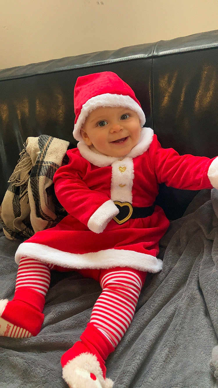 Lilas participe au concours pour gagner de l'argent avec cette photo : baby, child, santa_claus_costume, red_clothing, striped_leggings, smiling, indoor, couch, blanket, festive, holiday, cute, happy, portrait, infant, headwear, cozy, plush, person, seasonal
