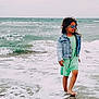 child, girl, beach, ocean, waves, sand, water, denim_jacket, dress, sunglasses, barefoot, smiling, curly_hair, summer, outdoor, sea, shore, nature, happy, playful