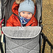 Logan is registered to the contest to win money with this photo: baby, blue_eyes, child, cozy, cute, fabric, face, hat, infant, jacket, outdoor, pavement, pom_poms, seatbelt, smile, stroller, transport, warm, wheel, winter_clothing