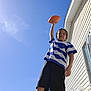 Braxton is registered to the contest to win money with this photo: child, boy, football, outdoor, sunny, blue_sky, house, window, shorts, striped_shirt, standing, confident, daylight, sunflare, casual_clothing, person, playing, summer, recreation, backyard