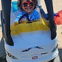 child, toy_car, sunglasses, outdoor, smiling, happy, sunny, playground, grass, sand, blue_sky, vehicle, small, cute, childhood, fun, casual_clothing, daytime, playing, young