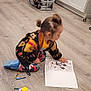 toddler, child, coloring_book, mickey_mouse, toys, stacking_rings, toy_car, hedgehog_game, wooden_floor, kitchen_cabinets, diaper_boxes, pampers, indoor, kneeling, play, coloring, hair_buns, casual_clothing, home, childhood