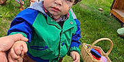 Braydon is registered to the contest to win money with this photo: child, toddler, outdoor, grass, bench, holding_hand, jacket, brown_pants, sneakers, basket, picnic, person, hair, face, expression, nature, daylight, people, greenery, casual_clothing