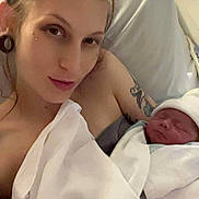 Oliver is registered to the contest to win money with this photo: mother, newborn, baby, hospital_bed, blanket, swaddle, woman, tattoo, piercing, bed, hospital, sleeping, infant, person, portrait, skin, headwear, indoor, parent, love