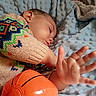 child, toddler, sleeping, sweater, colorful_clothing, blanket, blue_blanket, toy, basketball_toy, hand, face, cozy, indoor, rest, cute, soft_texture, knitwear, person, portrait, closeup