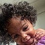 Nayla is registered to the contest to win money with this photo: child, toddler, curly_hair, smiling, face, portrait, indoor, skin, hand, purple_clothing, cute, baby, person, closeup, happy, young_child, head, expression, cheeks, curly
