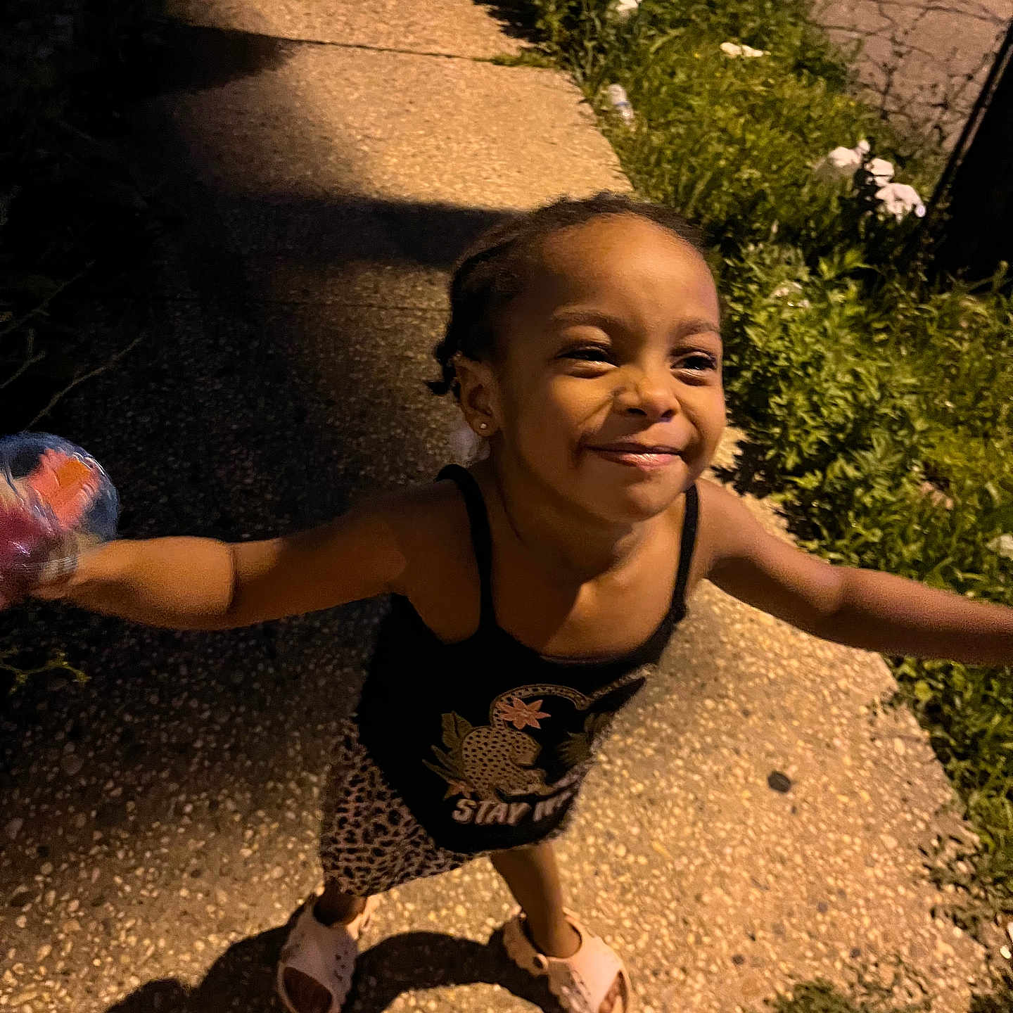 Blue joined the competition — help win amazing prizes! braids, casual, child, concrete, footwear, girl, grass, happy, holding_object, night, outdoors, patterned_skirt, person, plants, playful, shadow, sidewalk, sleeveless_top, smiling, streetlight