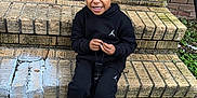 Blue joined the competition — help win amazing prizes! child, smiling, sitting, brick_steps, black_hoodie, black_pants, sneakers, outdoor, playful, person, hair_buns, grin, concrete, casual_clothing, young_child, urban, daylight, holding_object, texture, greenery