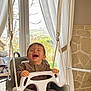 child, toddler, laughing, swing, indoor, window, curtains, seat, plastic, hands, smile, mouth_open, clothing, harness, stone_wall, greenery_outside, home_interior, playtime, happy, portrait