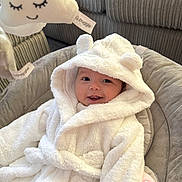 Nyla joined the competition — help win amazing prizes! baby, smile, hooded_robe, white_clothing, plush_toy, cloud_toy, cushion, indoor, cozy, soft_texture, child, infant, happy, face, person, cute, seated, pink_blanket, furniture, relaxing