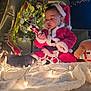 Bresman Jr is registered to the contest to win money with this photo: toddler, child, santa_claus_costume, christmas_lights, nutcracker, plush_toy, reindeer, holiday_decor, balloon, festive, indoors, celebration, christmas_tree, toy, curious, red_clothing, white_fur_trim, face, person, cozy