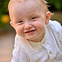 baby, child, smile, face, blue_eyes, light_hair, white_shirt, portrait, outdoor, garden, flower, blurred_background, happy, cute, infant, close_up, person, skin, head, childhood