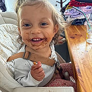 Isis a rejoint le concours — aidez-le/la à gagner de superbes lots ! child, chocolate, clothing, cup_with_straw, curtain, face, furniture, hair, happy, high_chair, indoor, kitchen, messy, person, seatbelt, smiling, snack, table, toddler, wooden_table