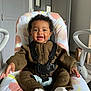 Kayla a rejoint le concours — aidez-le/la à gagner de superbes lots ! baby, infant, child, smiling, curly_hair, knitted_outfit, brown_clothing, white_socks, baby_chair, cushion, indoor, home, modern, happy, seated, person, cute, portrait, furniture, floor