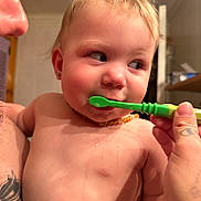 Ruby is registered to the contest to win money with this photo: baby, infant, child, portrait, face, eyes, blond_hair, smiling, toothbrush, toothbrushing, bathroom, indoor, adult_hand, caregiver, baby_teeth, bare_chest, necklace, close_up, candid, parenting