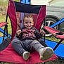 child, toddler, smiling, red_chair, outdoor, camping_chair, sweatshirt, casual_clothing, grass, car, blue_canopy, happy, person, seat, footwear, curly_hair, nature, daylight, relaxed, portrait