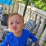 Kash joined the competition — help win amazing prizes! child, toddler, blue_clothing, outdoor, balustrade, patio_chair, greenery, potted_plant, curly_hair, playful, kiss, face, smiling, summer, daylight, person, hand, relaxing, casual, expression