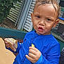 Kash is registered to the contest to win money with this photo: toddler, child, curly_hair, blue_jacket, sandwich, chip, outdoor, greenery, house, porch, expression, snack, hand, sitting, young_child, cute, daylight, face, person, casual_clothing