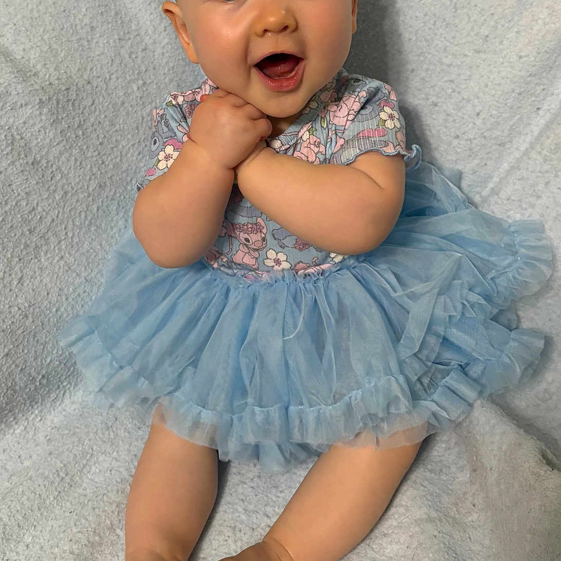 Evelyn is registered to the contest to win money with this photo: baby, barefoot, blanket, blue_tutu, child, clothing, cute, expressive_face, feet, hands, happy, headband, indoors, infant, light_background, portrait, sitting, smiling, soft_texture, young_child