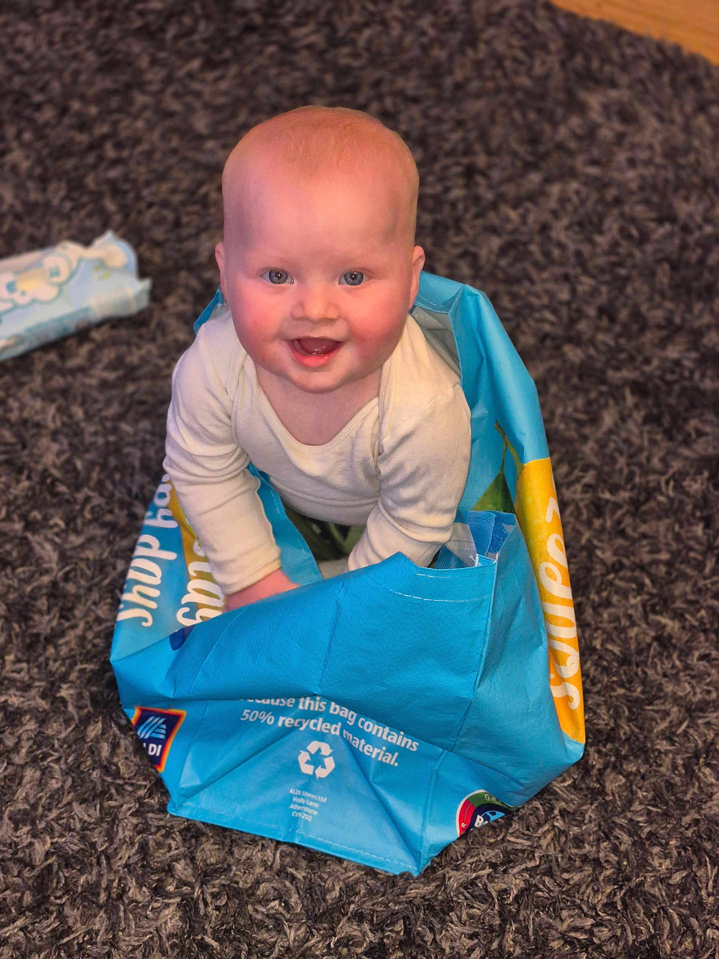 Palmer joined the competition — help win amazing prizes! baby, child, blue_bag, carpet, smiling, happy, indoor, cute, sitting, recycled_material, playful, person, floor, head, clothing, bright_eyes, rosy_cheeks, expression, fun, home