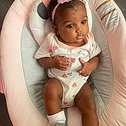 Destiny is registered to the contest to win money with this photo: baby, infant, child, onesie, headband, pink, heart_pattern, baby_seat, soft_furniture, socks, curly_hair, indoor, floor, cute, portrait, young_child, comfortable, expression, skin, hands