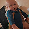 adult_hands, baby, blue_outfit, camcorder_style, child, eyes, face, furniture, home, indoor, infant, long_sleeves, photograph, portrait, retro, serious_expression, sitting, supported, timestamp, vintage