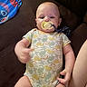 Tazz is registered to the contest to win money with this photo: arm, baby, child, closeup, clothing, couch, cozy, dinosaur, face, hand, head, home, indoor, infant, onesie, pacifier, portrait, sitting, smiling, toy