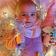 Sasha participe au concours pour gagner de l'argent avec cette photo : baby, tinsel, doll, pink, striped_clothing, soft_toy, infant, holiday_decor, cozy, smiling, face, cute, child, blanket, indoor, warm_lighting, festive, holding, toy, adorable