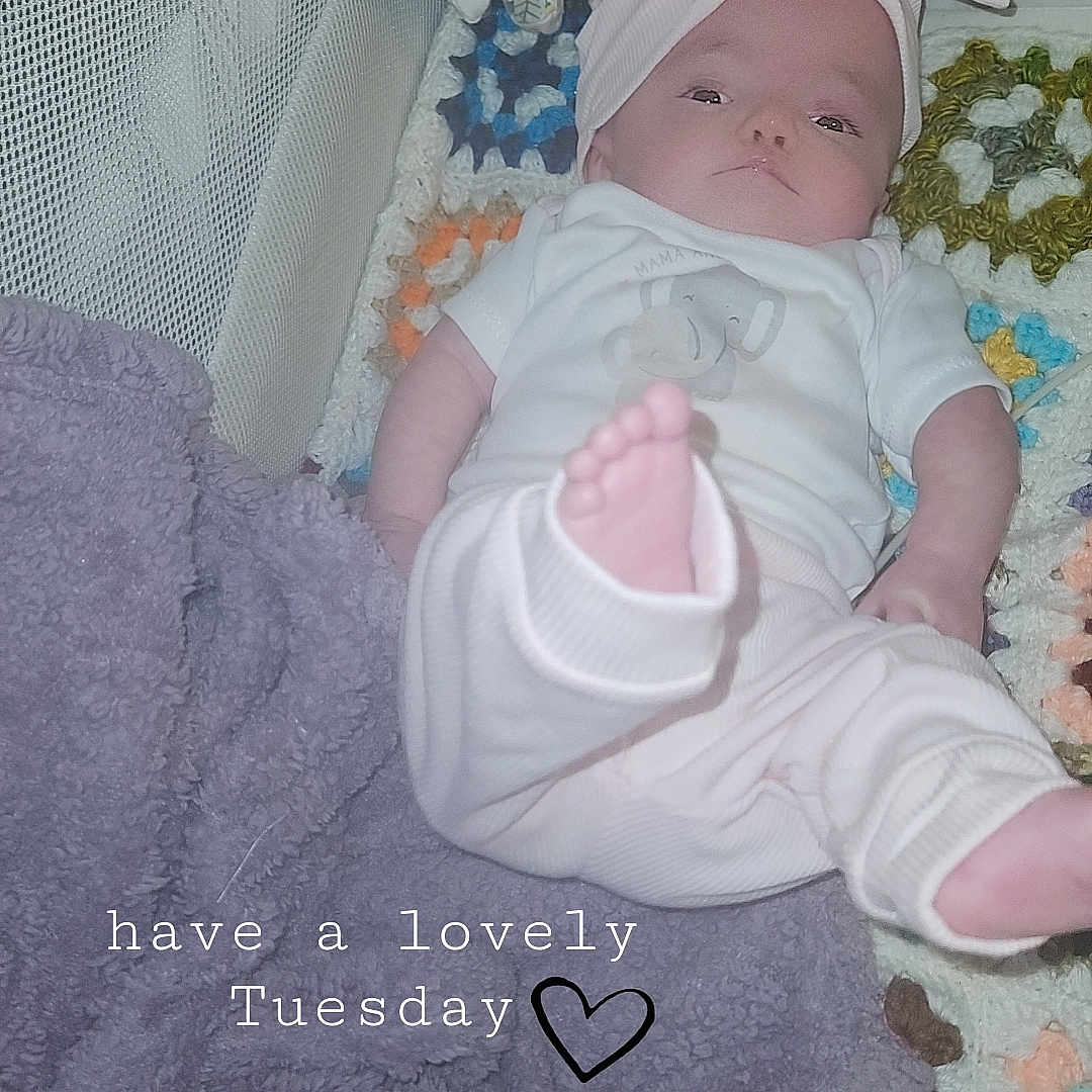 Evelyn is registered to the contest to win money with this photo: baby, infant, blanket, crochet, headband, bow, foot, towel, warning_sign, clothing, lying_down, indoors, cute, soft_toys, pastel_colors, cozy, child, text_overlay, calm, relaxed