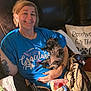 woman, smiling, puppy, dog, couch, blanket, pillow, tattoo, blue_tshirt, indoor, relaxing, cute, sleeping_dog, home, comfort, hand, face, person, leisure, pet