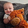 Elijah joined the competition — help win amazing prizes! baby, child, blue_eyes, smile, stuffed_animal, plush_toy, orange, couch, gray_cushion, indoor, happy, cute, portrait, infant, holding, soft_toy, home, wall_art, seated, cozy