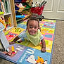 baby, child, smiling, playroom, rug, alphabet, toy, bookshelf, carpet, floor, indoor, colorful, clothing, bib, person, happy, infant, play, furniture, cute