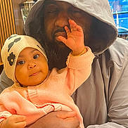 Marie joined the competition — help win amazing prizes! baby, adult, child, hoodie, hat, indoor, person, holding, cute, playful, face, hand, sweater, skin, closeup, warm_lighting, expression, interaction, love, family