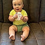 baby, child, infant, couch, brown, yellow_shirt, green_shorts, barefoot, holding_sign, eight_months, happy, cute, indoor, portrait, sitting, small_hands, blue_eyes, short_hair, plush, soft_lighting