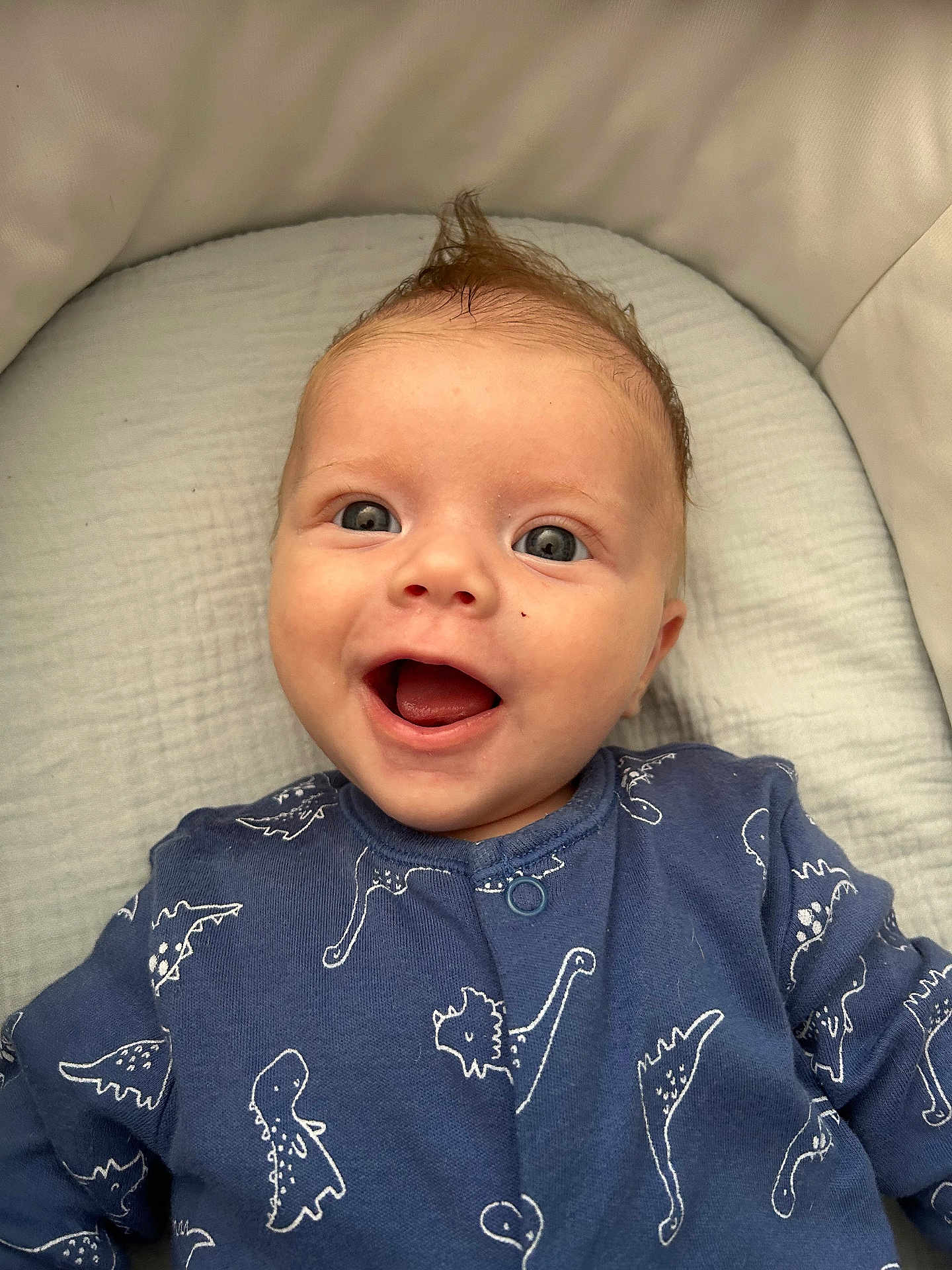 Armand a rejoint le concours — aidez-le/la à gagner de superbes lots ! baby, infant, smile, happy, blue_onesie, dinosaur_pattern, hair_tuft, face, eyes, cushion, soft, lying_down, child, cute, closeup, portrait, clothing, baby_clothes, indoors, person