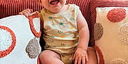 Louis a rejoint le concours — aidez-le/la à gagner de superbes lots ! baby, smiling, infant, couch, pillows, decorative_pillows, onesie, patterned_clothing, happy, sitting, indoor, home, cozy, child, cute, face, furniture, texture, light, room