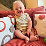 baby, smiling, infant, couch, pillows, decorative_pillows, onesie, patterned_clothing, happy, sitting, indoor, home, cozy, child, cute, face, furniture, texture, light, room