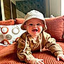 Louis a rejoint le concours — aidez-le/la à gagner de superbes lots ! baby, child, smiling, hat, crawling, sofa, couch, living_room, orange, beige, clothing, happy, face, person, indoor, pillow, patterned_wallpaper, wooden_door, texture, curious