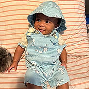 Taylor joined the competition — help win amazing prizes! baby, child, smiling, blue_clothing, bucket_hat, bunny_print, striped_bedspread, bed, dog, pet, sock, cute, indoor, happy, person, infant, portrait, sitting, animal, cozy