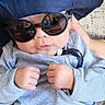 baby, infant, sunglasses, hat, blue_hat, gray_outfit, clothing, person, face, headwear, fist, close_up, indoor, cute, child, fashion_accessory, cool, portrait, young, wearing