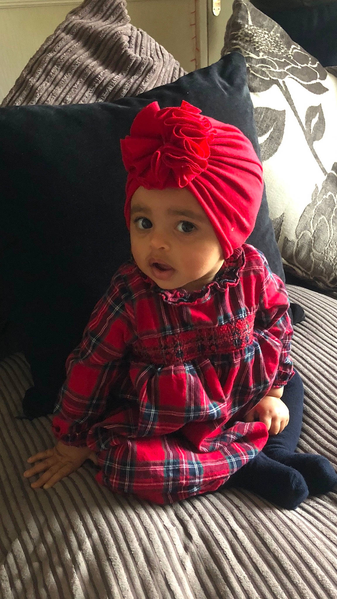 Lottie is registered to the contest to win money with this photo: baby, baby_toddler_clothing, cap, child, christmas, christmas_eve, facial_expression, flooring, headwear, knit_cap, magenta, pattern, person, plaid, red, skin, sleeve, smile, tartan, toddler