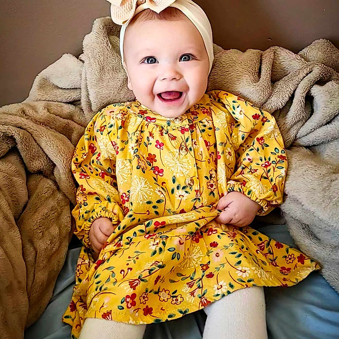 Willow is registered to the contest to win money with this photo: baby, babylaughing, blanket, clothing, coat, face, happy, head, laughing, person, sitting, smile