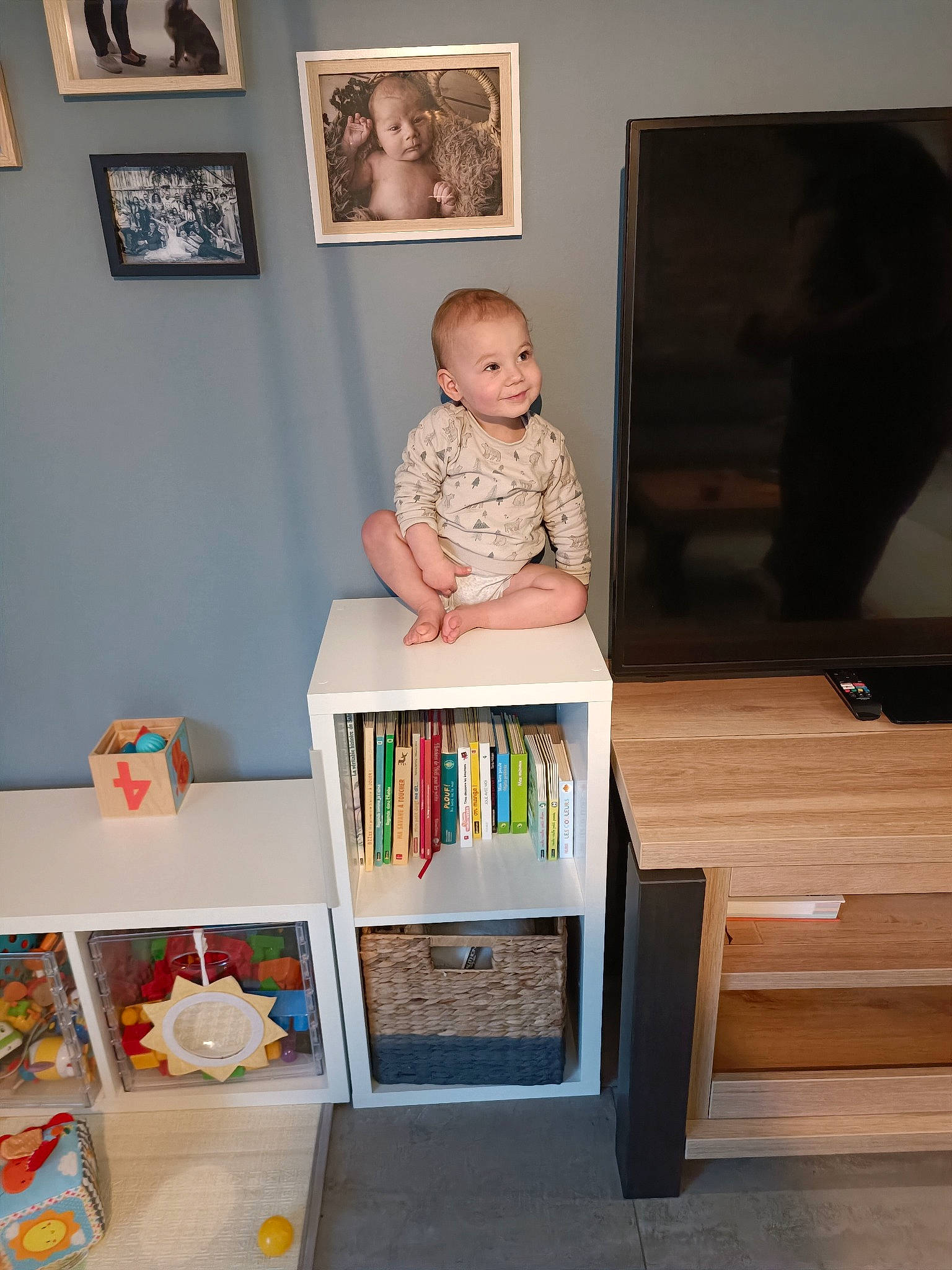 Noé participe au concours pour gagner de l'argent avec cette photo : baby, book, child, event, flooring, hardwood, interior_design, joy, living_room, person, picture_frame, rectangle, room, shelf, shelving, sitting, table, toddler, varnish, wood