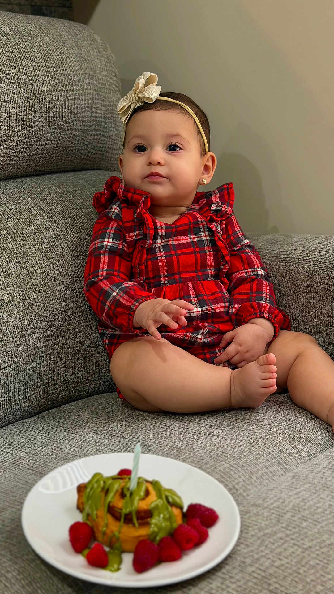 Gianna is registered to the contest to win money with this photo: baby, child, girl, plaid_dress, headband, bow, couch, gray_couch, plate, dessert, candle, raspberries, food, sitting, indoor, cute, portrait, celebration, holiday, happy