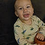 Kade is registered to the contest to win money with this photo: baby, child, dinosaur_pajamas, tongue_out, sitting, couch, blanket, cup, happy, indoors, infant, playful, smiling, person, young_child, clothing, face, hand, furniture, cute