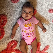 Zaniyah is registered to the contest to win money with this photo: baby, carpet, child, cute, face, floor, happy, indoors, infant, lying_down, onesie, patterned_rug, person, pink_clothing, playful_text, portrait, small_hair_tuft, smiling, soft_texture, young_child