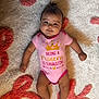 baby, carpet, child, cute, face, floor, happy, indoors, infant, lying_down, onesie, patterned_rug, person, pink_clothing, playful_text, portrait, small_hair_tuft, smiling, soft_texture, young_child