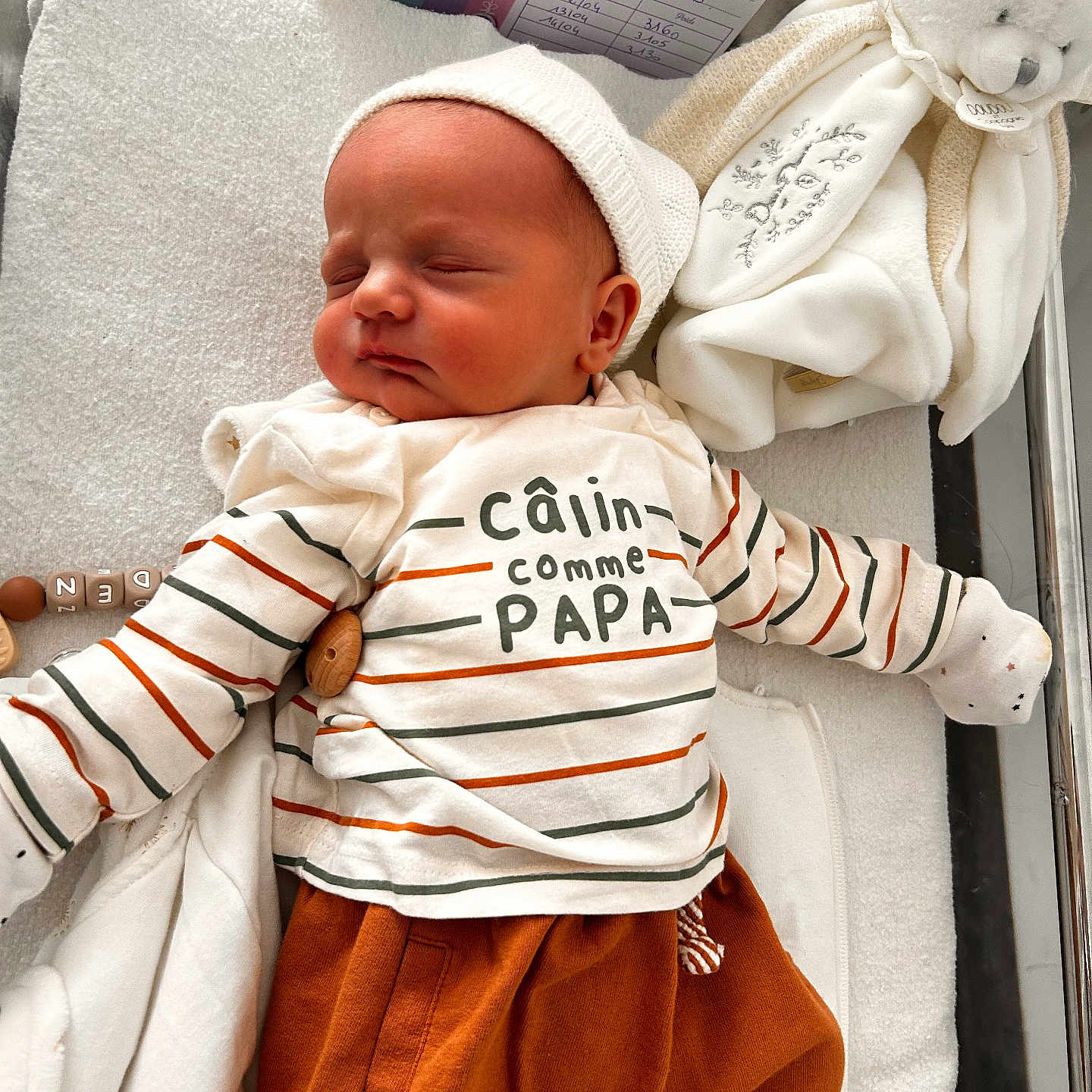 Eden a rejoint le concours — aidez-le/la à gagner de superbes lots ! newborn, baby, sleeping, striped_shirt, orange_pants, plush_toy, blanket, crib, cozy, cute, infant, child, resting, soft_toy, white, toddler, peaceful, indoors, warm_clothing, face